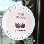 Naklejka na drzwiach salonu z hasłem „Dobieramy, nie oceniamy” i napisem „Miejsce przyjazne kobietom”
