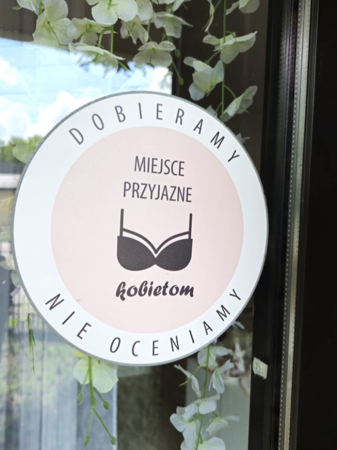 Naklejka na drzwiach salonu z hasłem „Dobieramy, nie oceniamy” i napisem „Miejsce przyjazne kobietom”